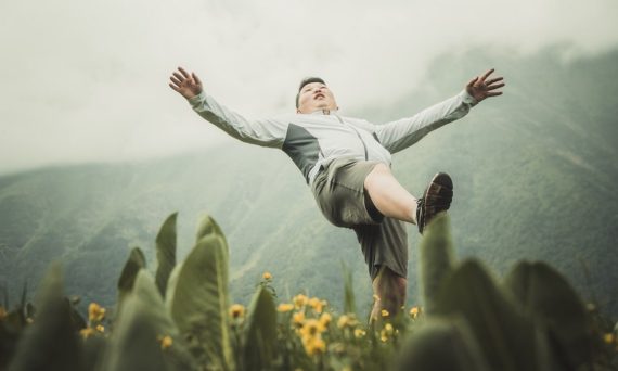 woman in white long sleeve shirt and black pants jumping on green grass field during daytime